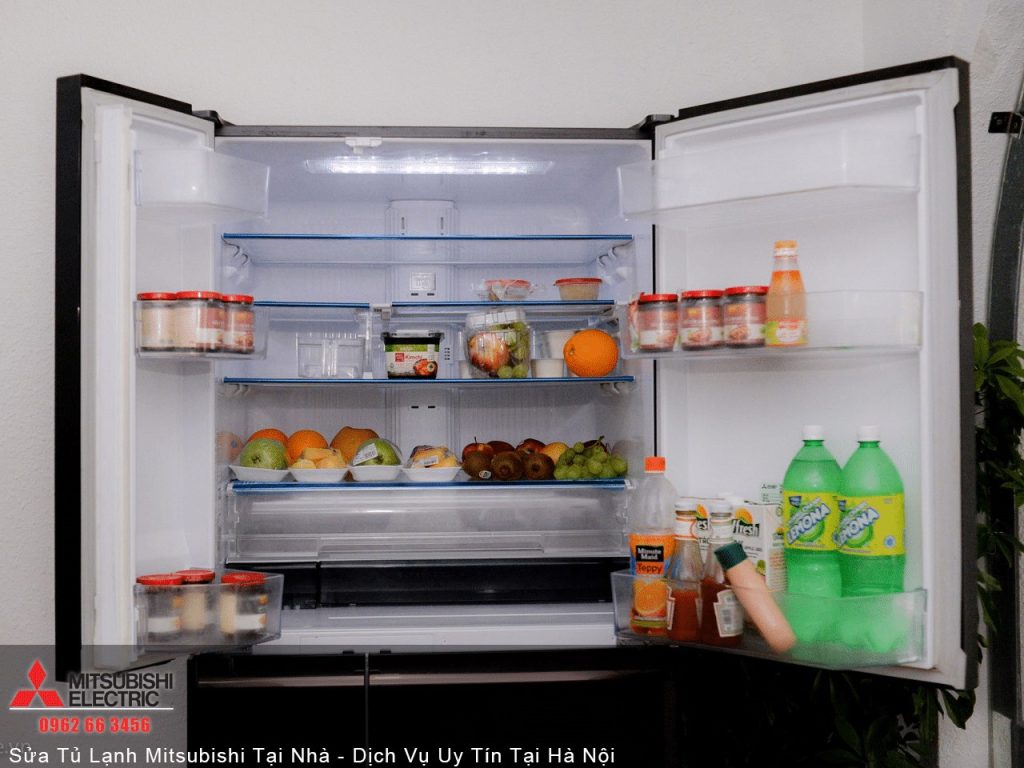Refrigerator with open door filled with fruits, vegetables, beverages, and food containers in a home kitchen setting.